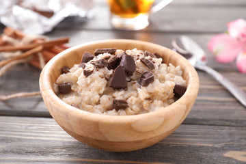 Bowl with tasty oatmeal and chocolate on wooden background