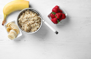 Bowl with tasty oatmeal, banana and strawberries on table