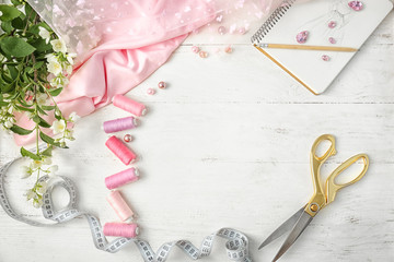 Frame made of color threads and sewing accessories on white wooden background