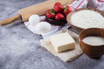 Baking ingredients for cake, pie, shortbread pastry: flour, eggs, sugar, butter, rolling pin and on gray concrete table background. Top view, copy space