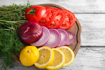 Board with different fresh herbs, lemon and vegetables on wooden background