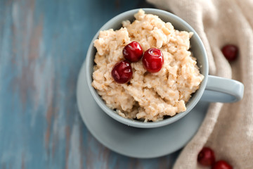 Tasty oatmeal with cherries in cup on table