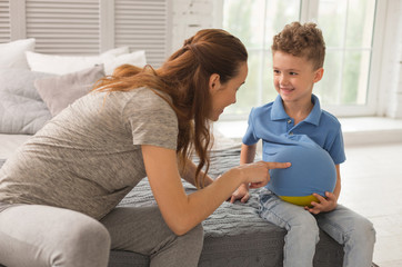 Entertaining son. Appealing dark-haired pregnant expecting woman feeling extremely happy while...