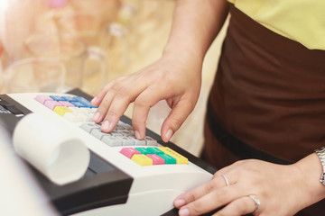 Sales women entering amount on cash register in offee shop