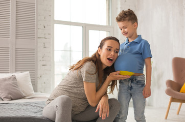 Amusing son. Pregnant beautiful woman amusing her little son while putting yellow ball under his...