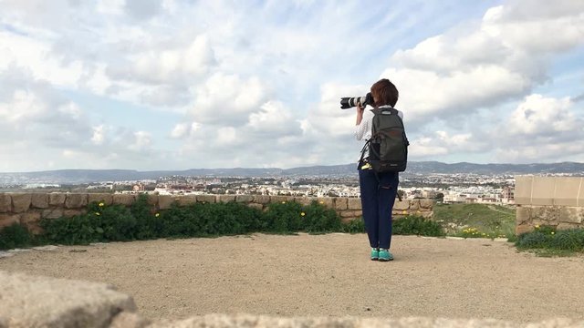 Young woman professional photographer taking pictures of the landscape and the Paphos city at Cyprus.