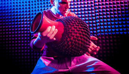 Young man playing on djembe in sound recording studio.