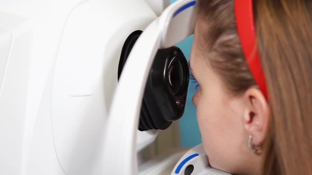 Close up shot of a young girl sitting at the ophthalmologist's office. Scanning her cornea using professional equipment.