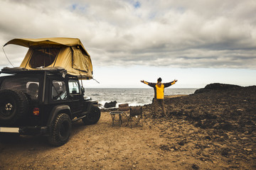 Fototapeta na wymiar adventurer man in journey travel with off road car and roof tent to enjoy freedom and explorer concept. discover the world living near the power of the nature. ocean coast home view. 