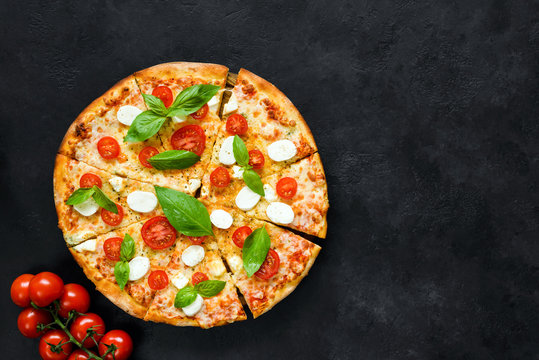 Hot italian pizza with tomatoes, basil and mozzarella on black stone background. Copy space for text