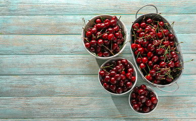 Bowls and basket with tasty cherries on wooden table