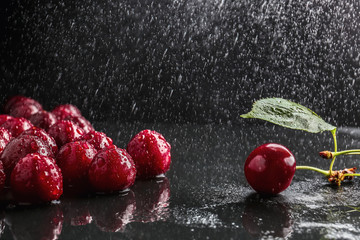 Tasty cherries with water drops on wet table against dark background