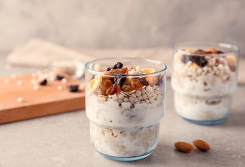 Tasty oatmeal dessert with almonds and dried fruits in glass on grey table
