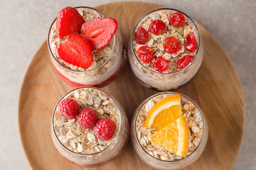 Wooden tray with tasty oatmeal desserts in glasses on light background