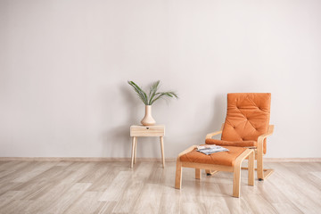 Living room with armchair, stand and green leaves in vase near light wall