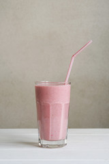 homemade strawberry smoothie or milk shake in glass with drinking straw on table, vertical background with copy space