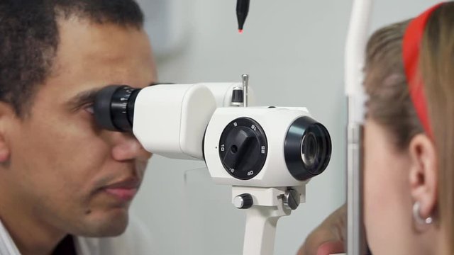 Close up shot of a male doctor using slit lamp biomicroscopy. Examining little girl's eyes at the office.