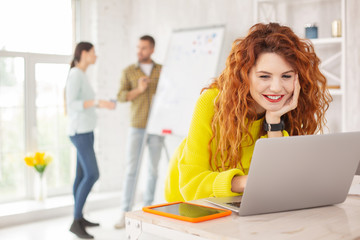 Era of digitalization. Cheerful female employee typing on laptop and smiling