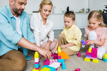 happy parents with cute little children playing with colorful blocks at home