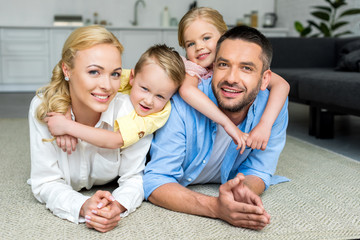 happy family lying on carpet and smiling at camera at home
