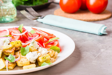 Fried zucchini with feta cheese, tomatoes, herbs and onions on a plate on a table