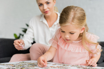 adorable little child playing with puzzle pieces while mother sitting behind