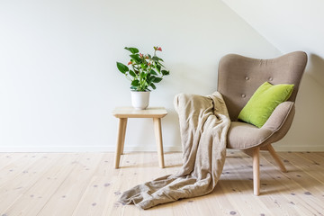 Beige armchair with a green pillow, blanket and a wooden table with a potted plant (Anthurium)....