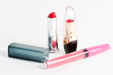 Two trendy red lipsticks and fashionable pink lip gloss on white
