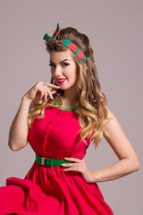 Smiling girl in red dress with hairdo poses in grey studio, pin up style