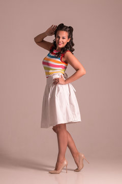 Pretty woman in skirt with hairdo poses in grey studio, pin up style, full body