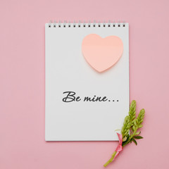 Composition with flowers and notebook on pink background. Flat lay. hand writing - be mine...