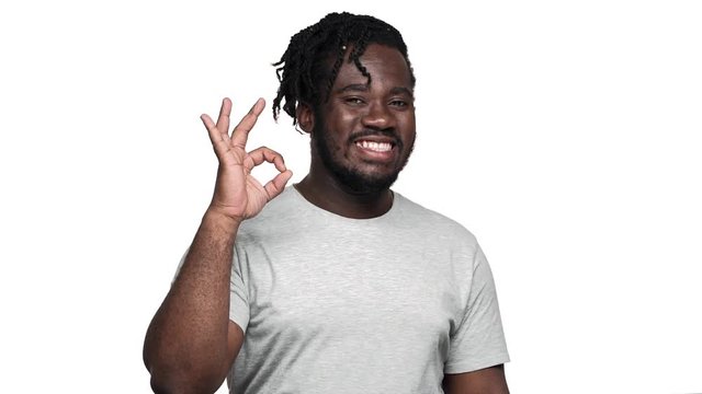Portrait of big african american man wearing afro hairdo and mustache showing alright sign with positive look, isolated over white background slow motion. Concept of emotions