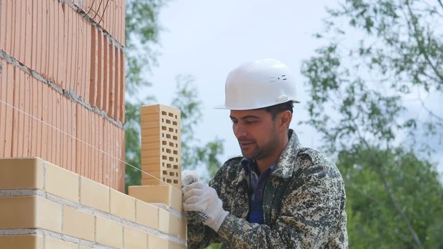 Bricklayer Builder aligns wall of bricks by using rope