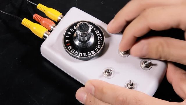 A hand operating a box: shifting and turning a rotary gear dial, switching and pressing button levers. Medium shot.

