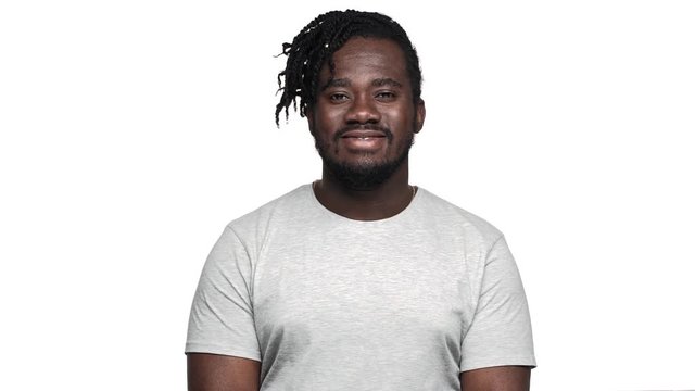 Portrait of adult dark skinned man 30s in casual t-shirt winking and nodding in agreement meaning yes or agree, isolated over white background slow motion. Concept of emotions