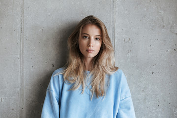 Pretty young girl in sweatshirt standing over gray wall