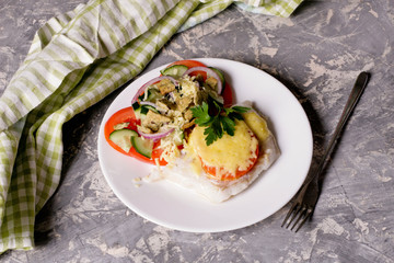 Fish baked with cheese and tomatoes on a white plate