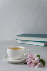 A cup of tea with apple blossom and books in the background