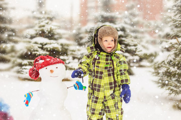 Funny little boy in a winter park with a snowman.