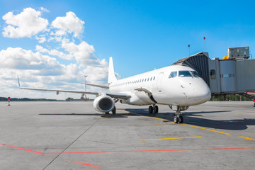 Naklejka premium Komercyjny samolot pasażerski na parkingu przy lotnisku z dziobem do przodu i trapem.