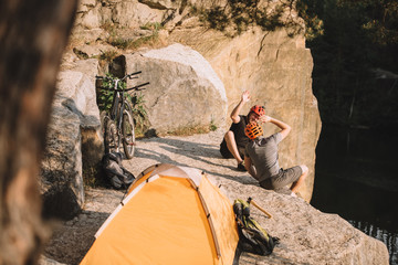 high angle view of active trial bikers sitting on rocky cliff with camping tent and giving high five