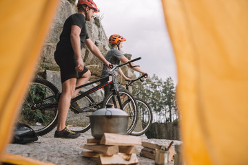 view of athletic trial bikers on rocky cliff outdoors from camping tent