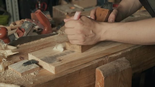 Slow motion - skilled craftsman carpenter whittles workpiece of wooden board with jack-plane in a workshop. Making handmade furniture.