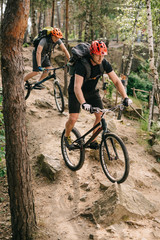 Fototapeta na wymiar extreme young trial bikers riding downhill on back wheels at beautiful forest