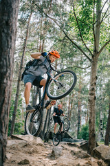 Fototapeta premium young trial bikers riding on back wheels at beautiful forest