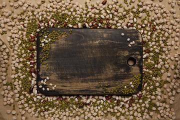 Old black cutting board on crumpled brown paper with chickpea, moong dal and kidney beans. Top...
