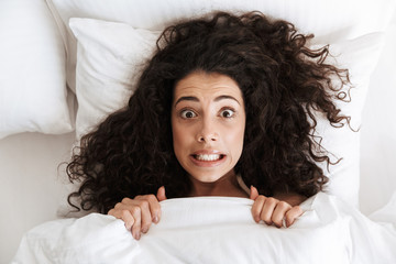 Photo from above of amusing uptight woman 20s with dark curly hair grimacing at camera, lying in...