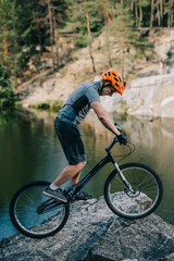 Fototapeta premium young trial biker balancing on rocky cliff over lake