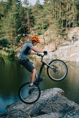 Fototapeta na wymiar athletic trial biker balancing on back wheel on rocky cliff over lake