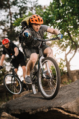 Obraz premium active young trial bikers riding on rocks at pine forest